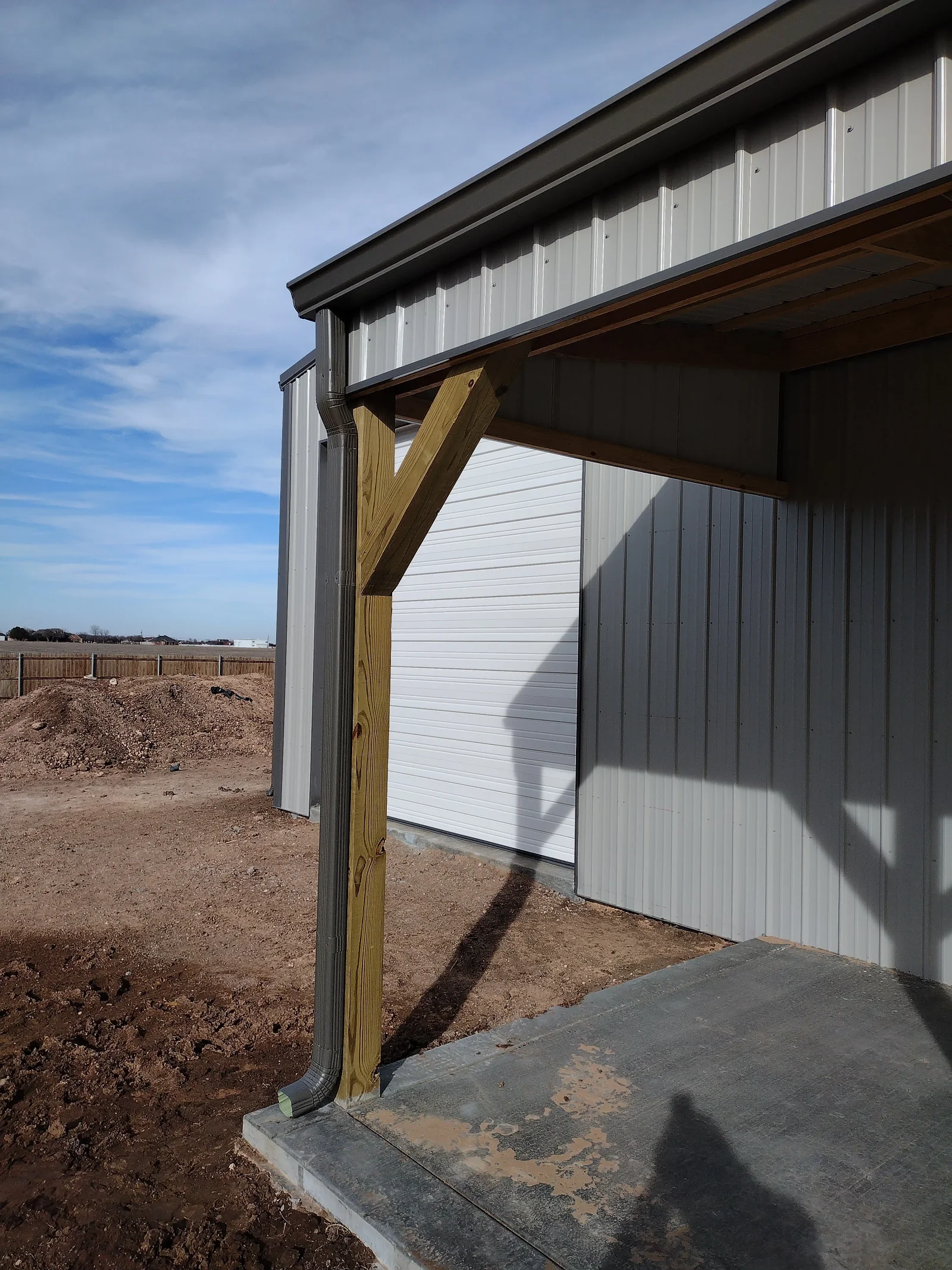 Metal building with white corrugated roof, charcoal siding, timber carport posts, and white garage door