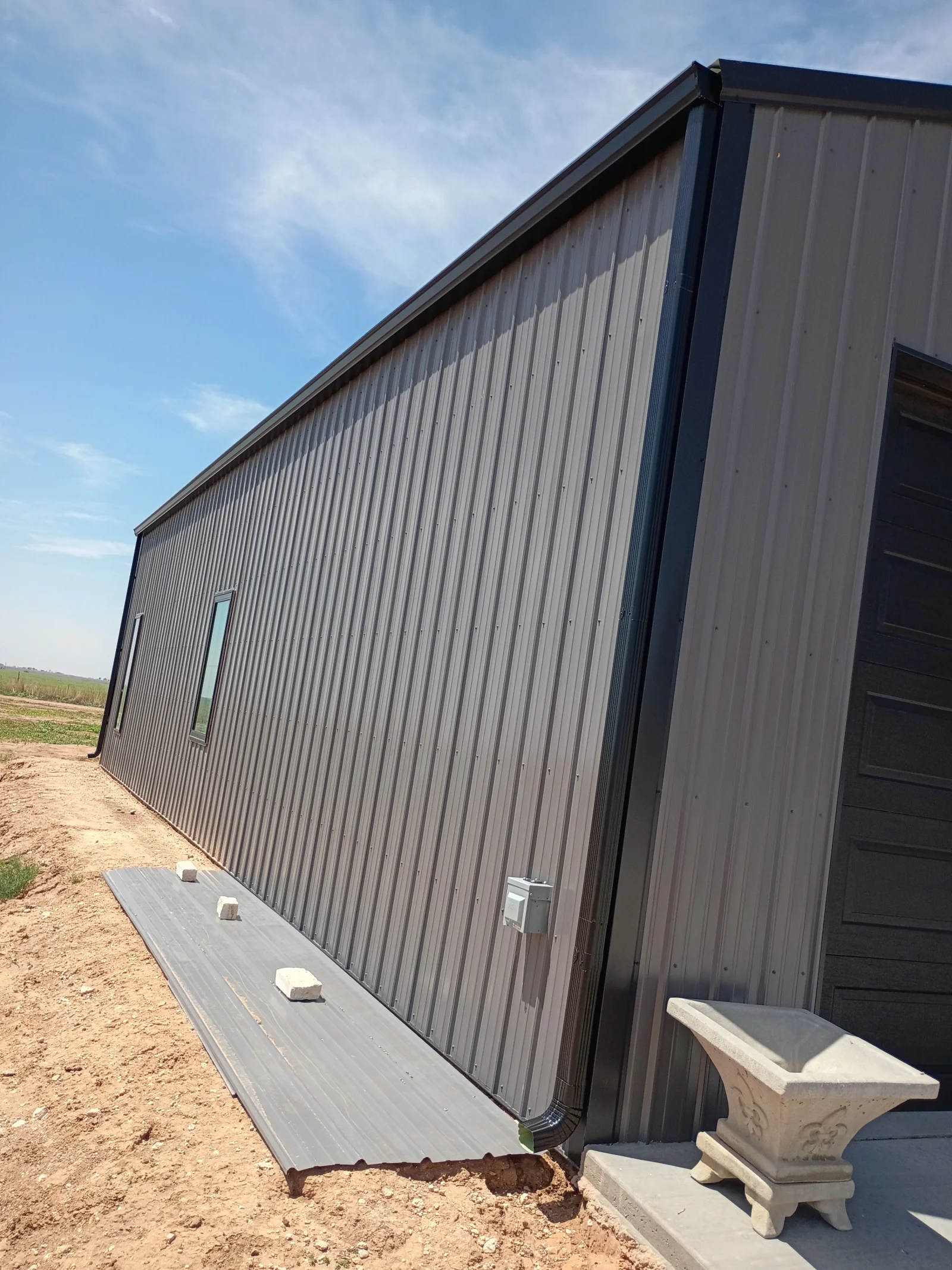 Metal building with vertical corrugated siding, standing seam roof, concrete foundation, and entry door