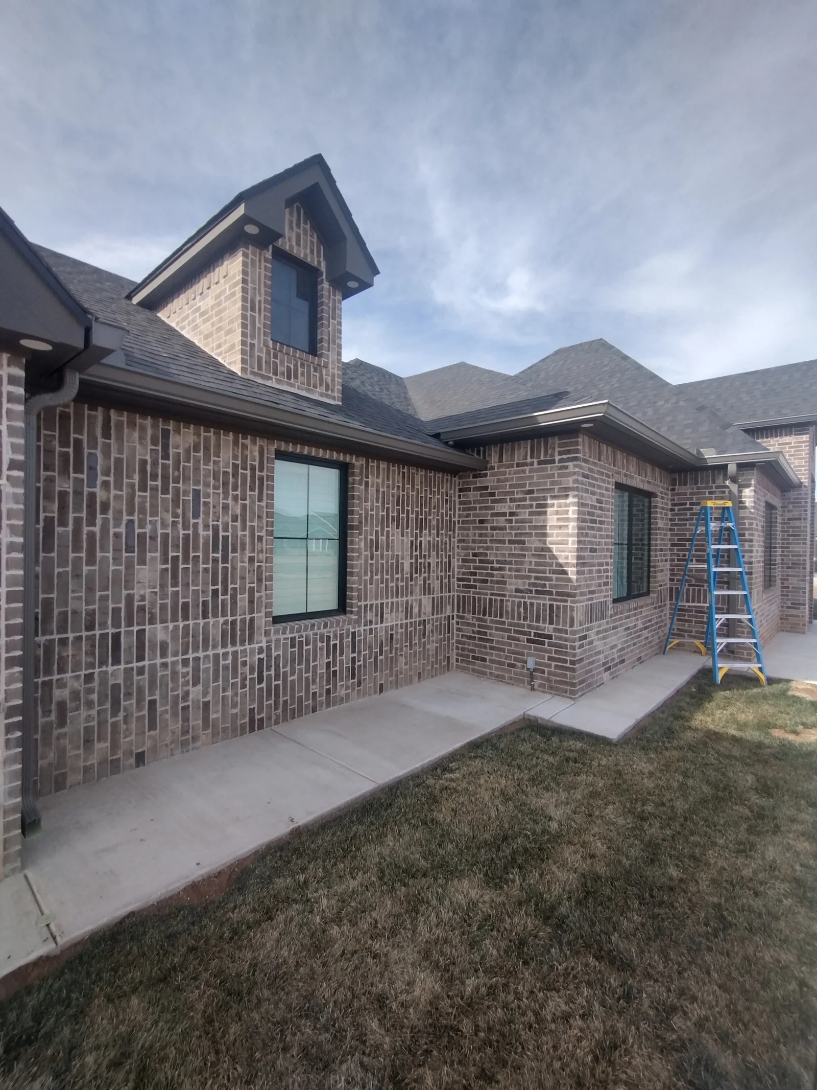 New brick home with multi-plane asphalt shingle roof and gable tower, professional installation visible