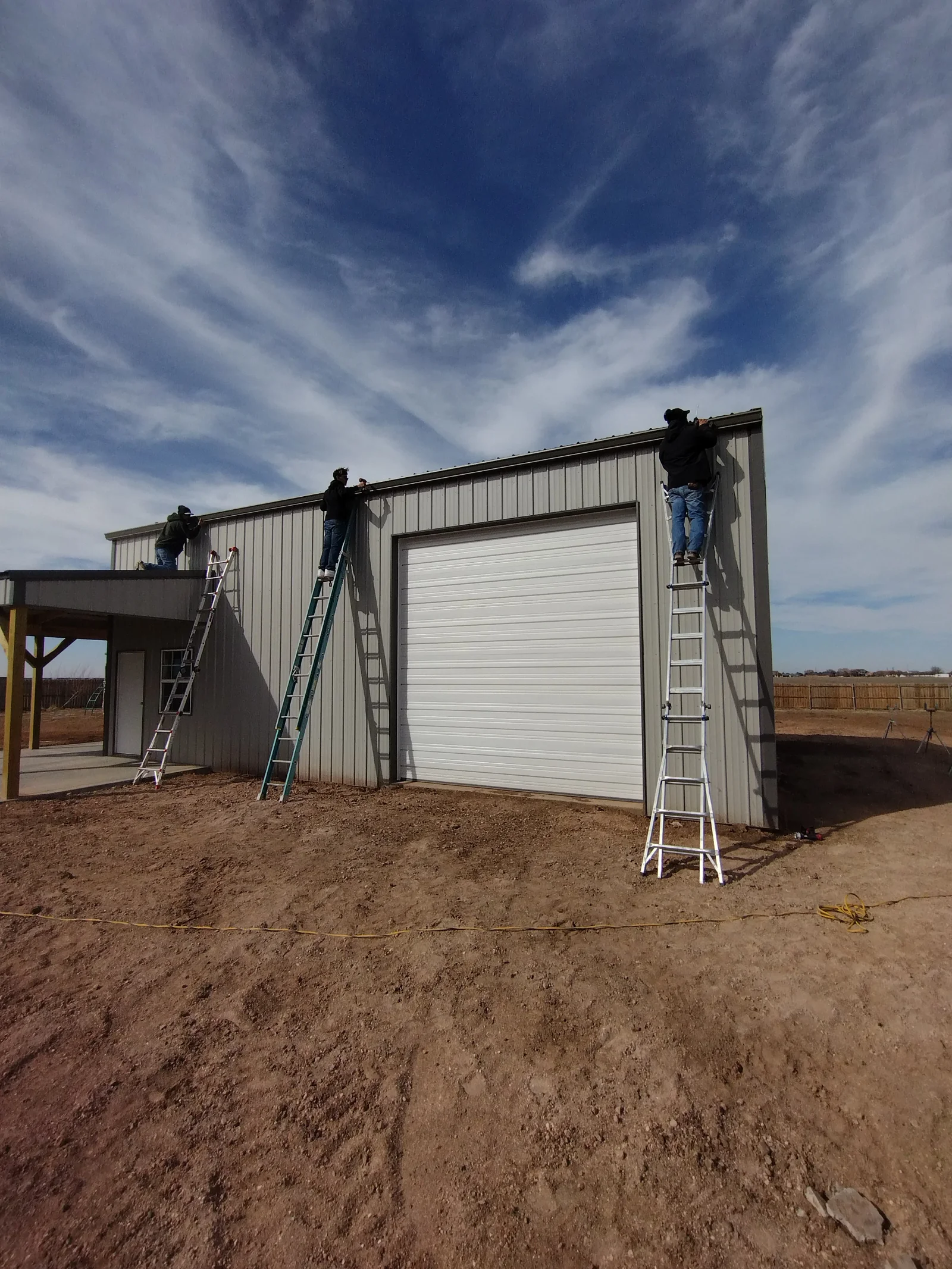 Workers installing standing seam metal roofing on commercial metal building with white garage door