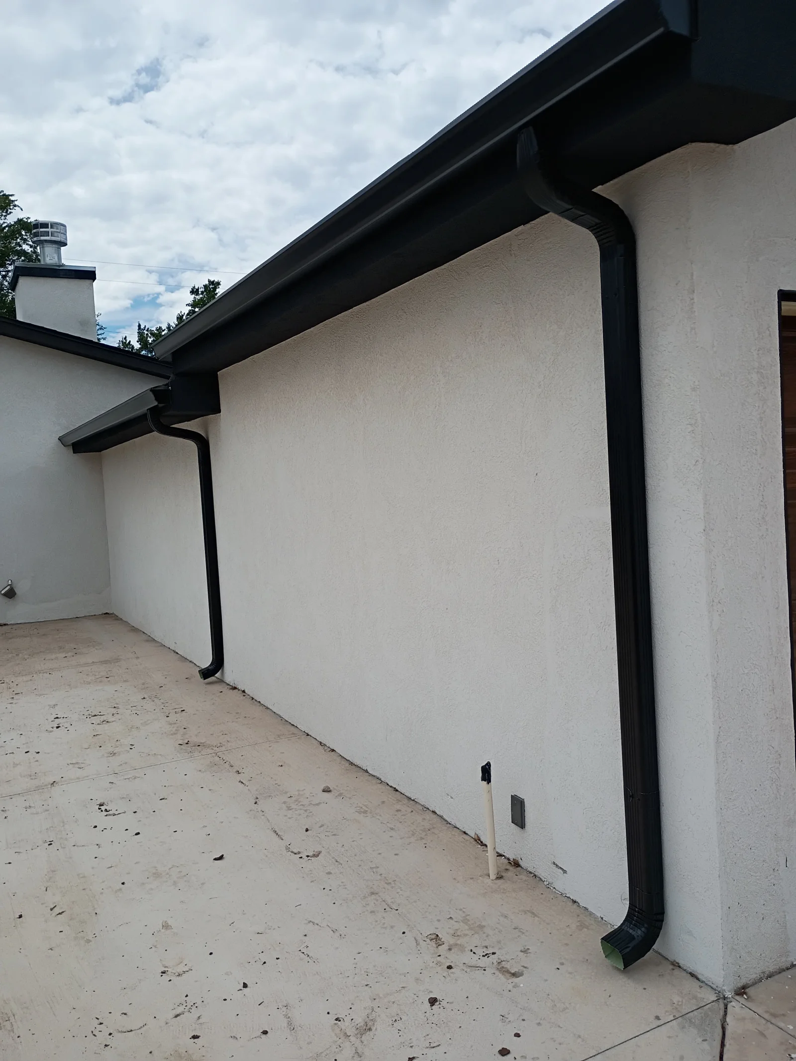 Black aluminum gutters and downspout on white stucco exterior wall
