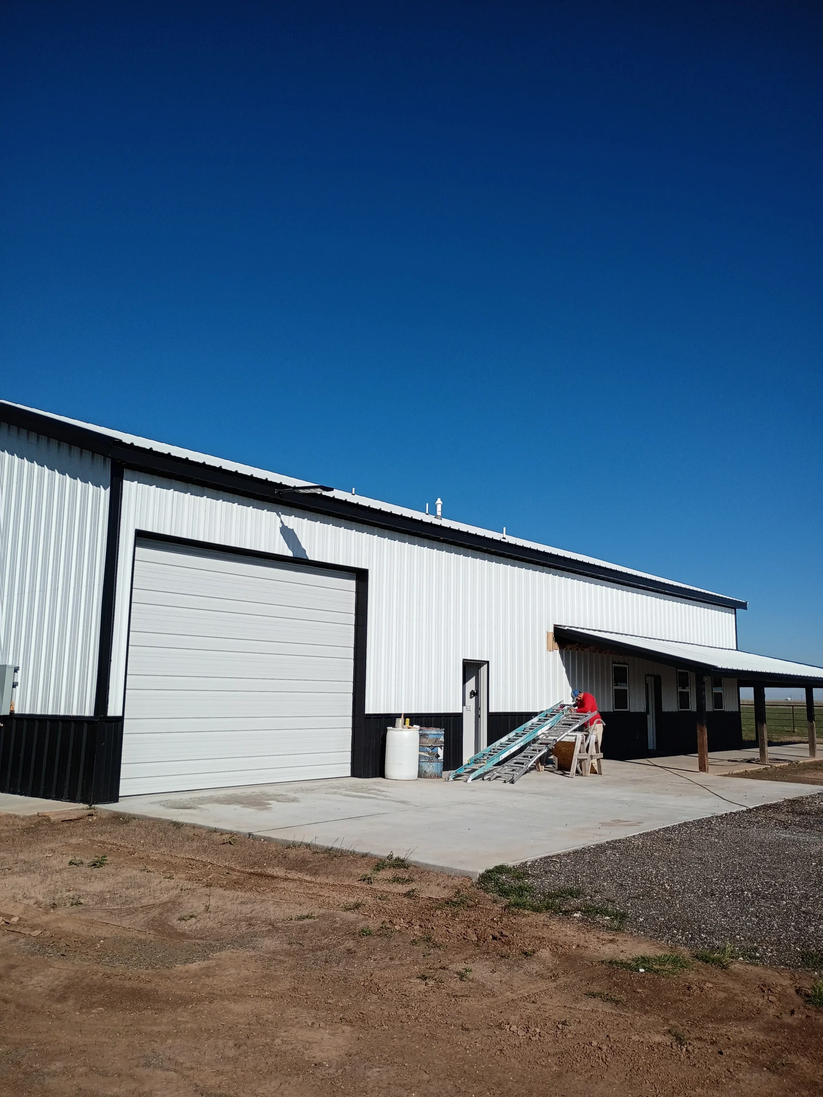 Metal building with white corrugated roof panels, black trim, and concrete foundation pad