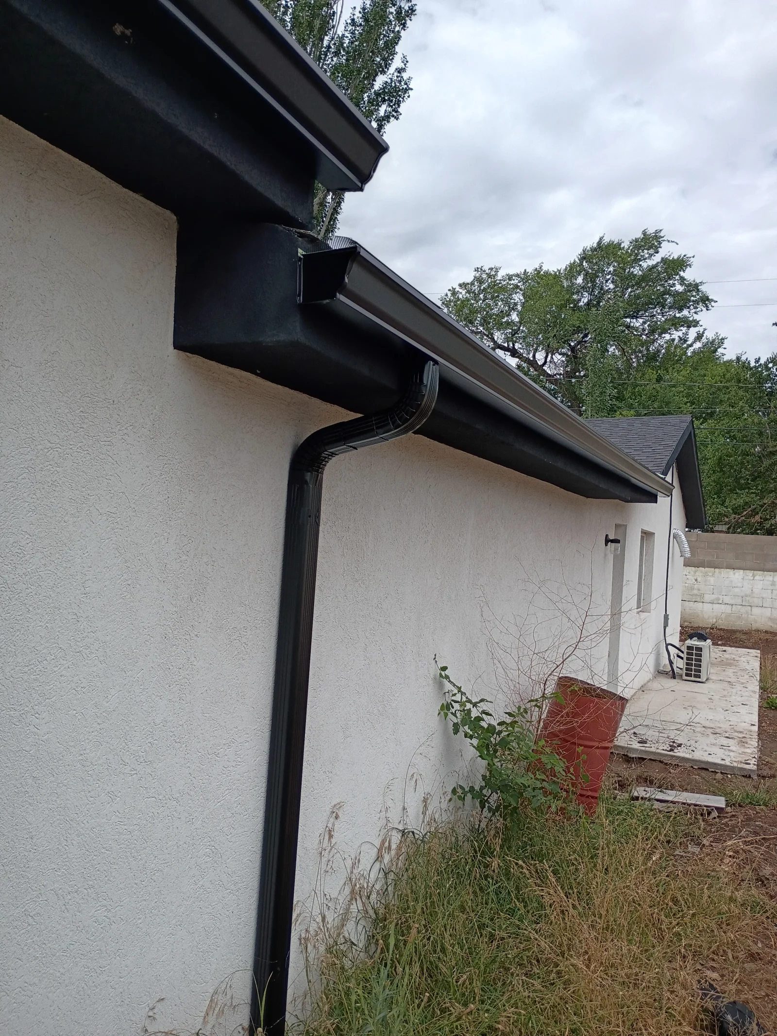 Black seamless gutters and downspout installed on white stucco residential building