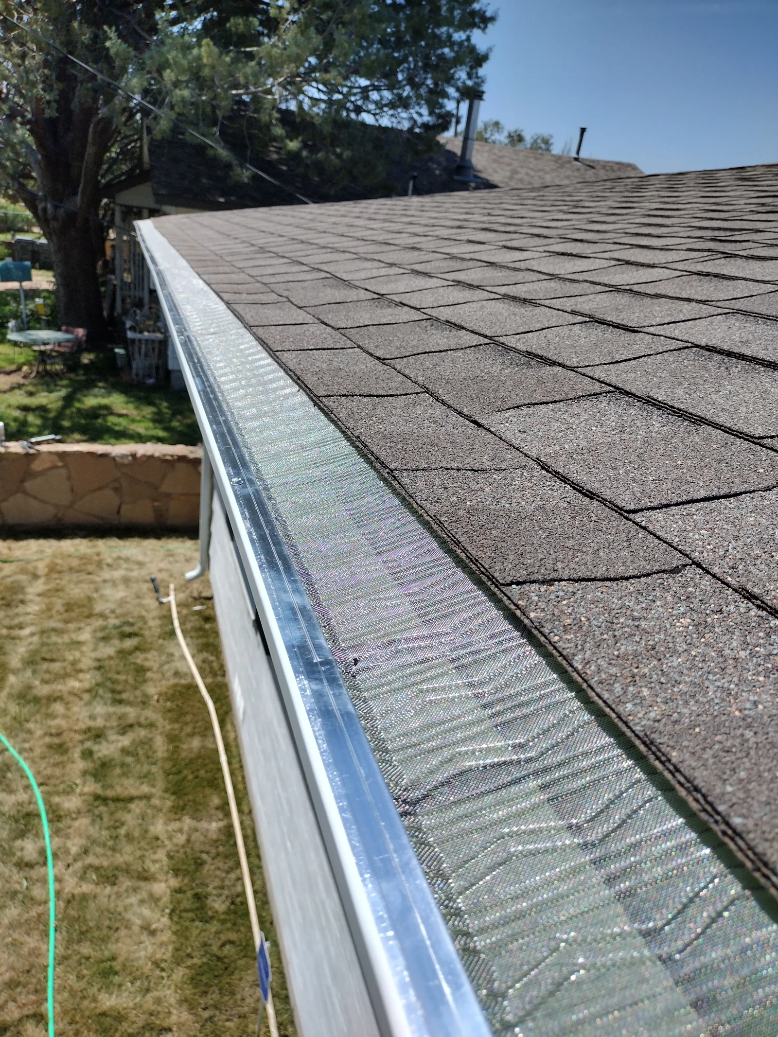 White aluminum gutter with mesh guard installed along roofline next to asphalt shingles