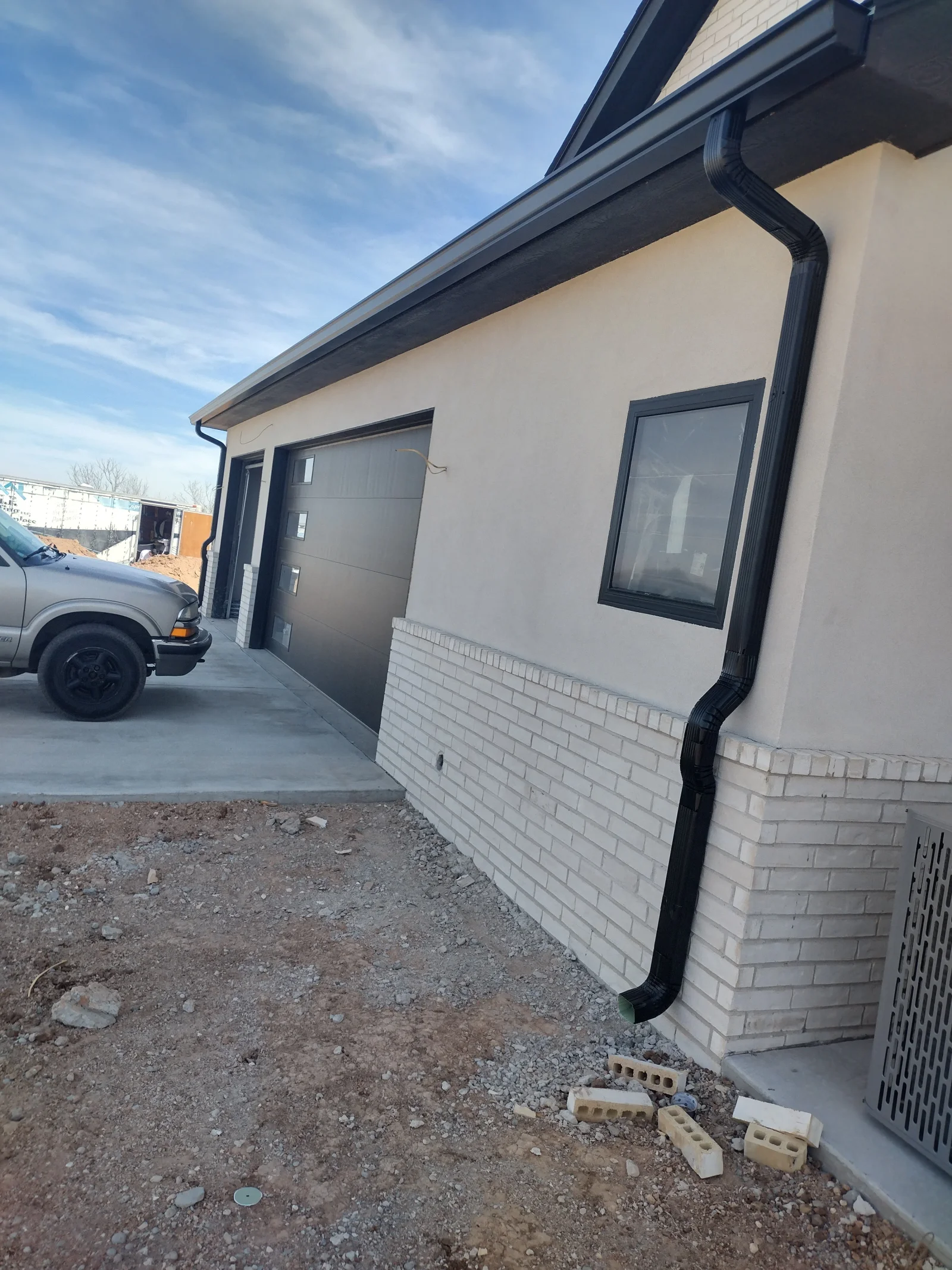 Black aluminum gutters and downspouts installed on white brick residential addition with black fascia trim