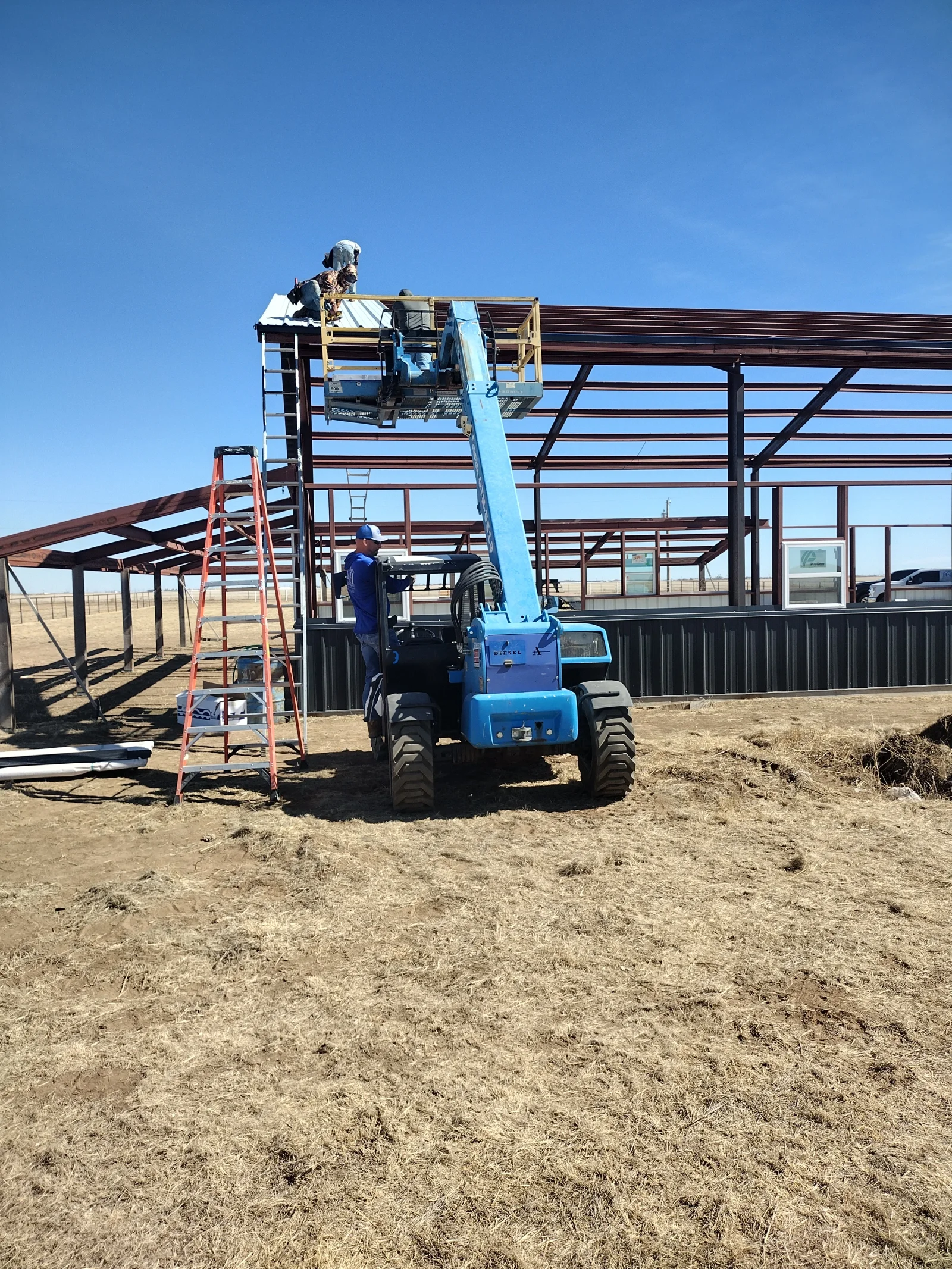 Metal roofing installation on agricultural building using elevated lift and work platform