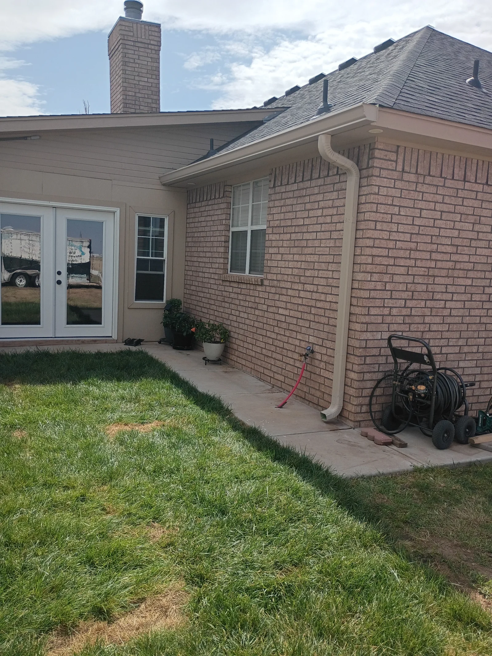 Tan seamless gutters and downspout installed on brick home exterior
