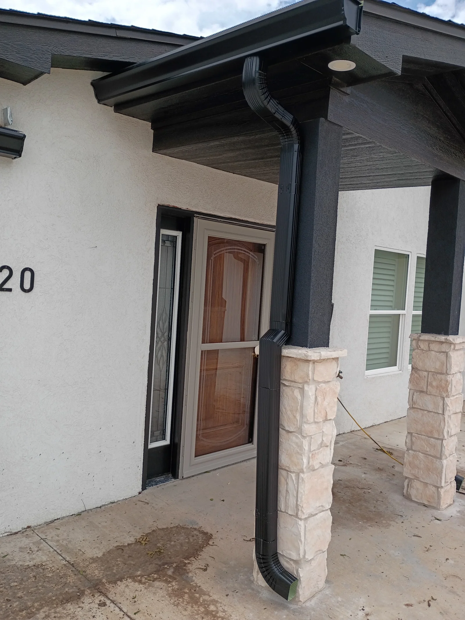 Black aluminum gutter and downspout installation on front entry overhang with stone pillars