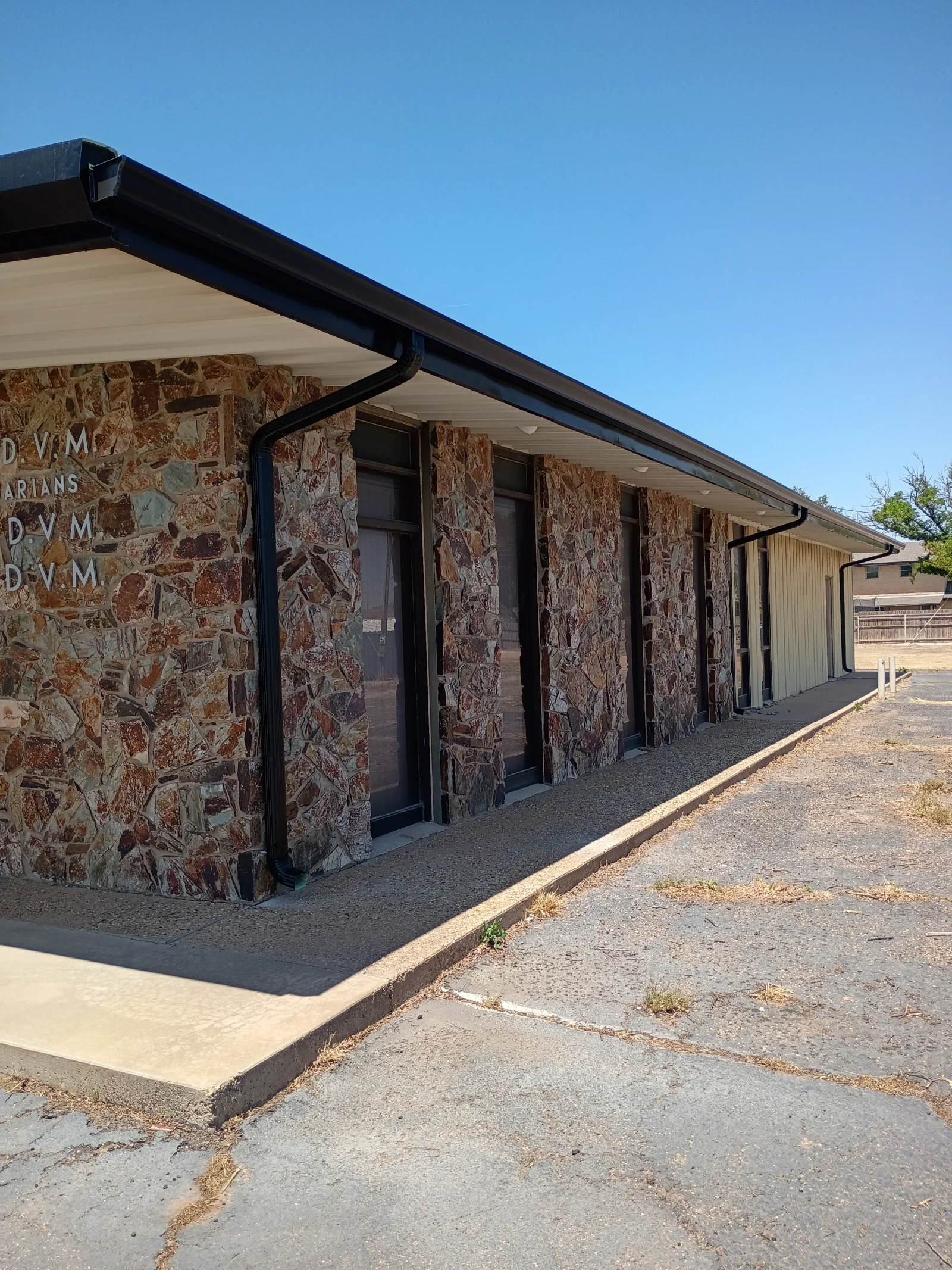 Black aluminum gutters and soffit on stone facade building with cream-colored soffit panels