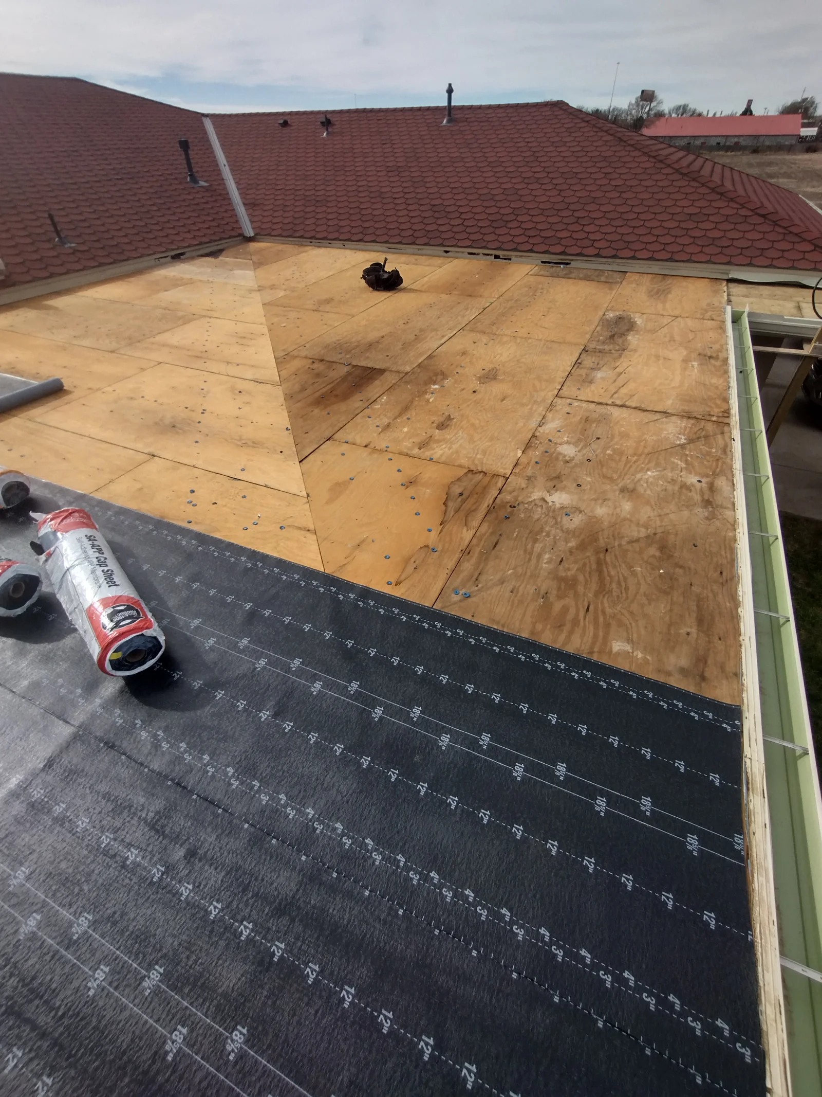 Roof replacement in progress with plywood decking, black underlayment, and burgundy shingles installed