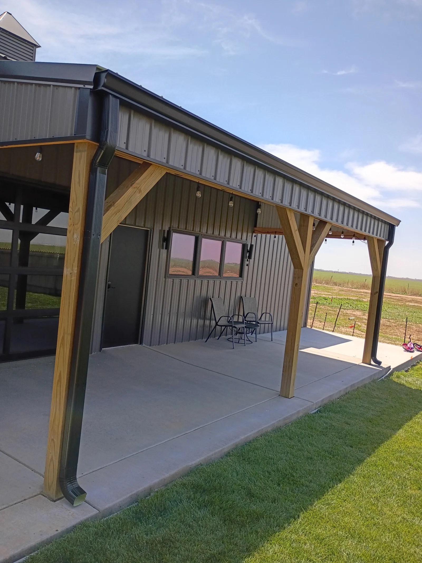 Metal building with standing seam roof, timber beams, metal siding, and concrete patio