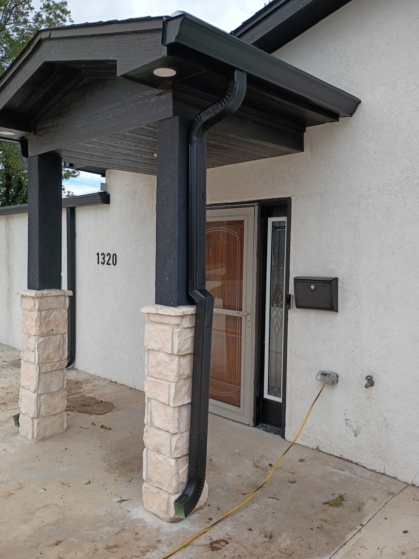 Black aluminum gutter and downspout on modern entry canopy with stone pillars